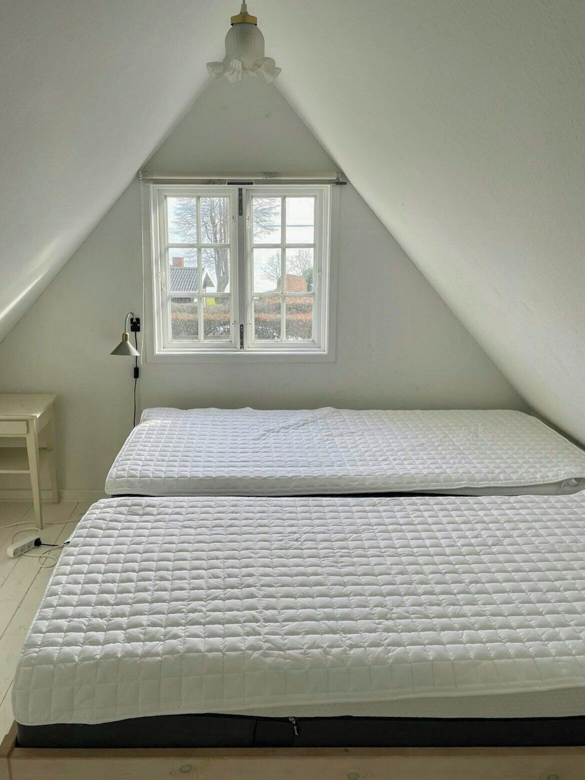 Une chambre avec deux lits, une fenêtre, un bureau et un luminaire au plafond.