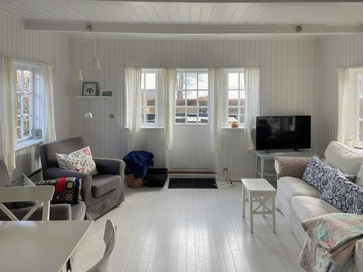 A living room with a sofa, a television, a dining table, and a window with curtains.