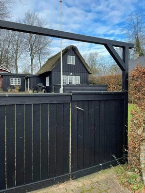 A black wooden fence with a metal gate, a house with a thatched roof, and a clear sky. - Thatched wooden house with sea view (Haderslev)