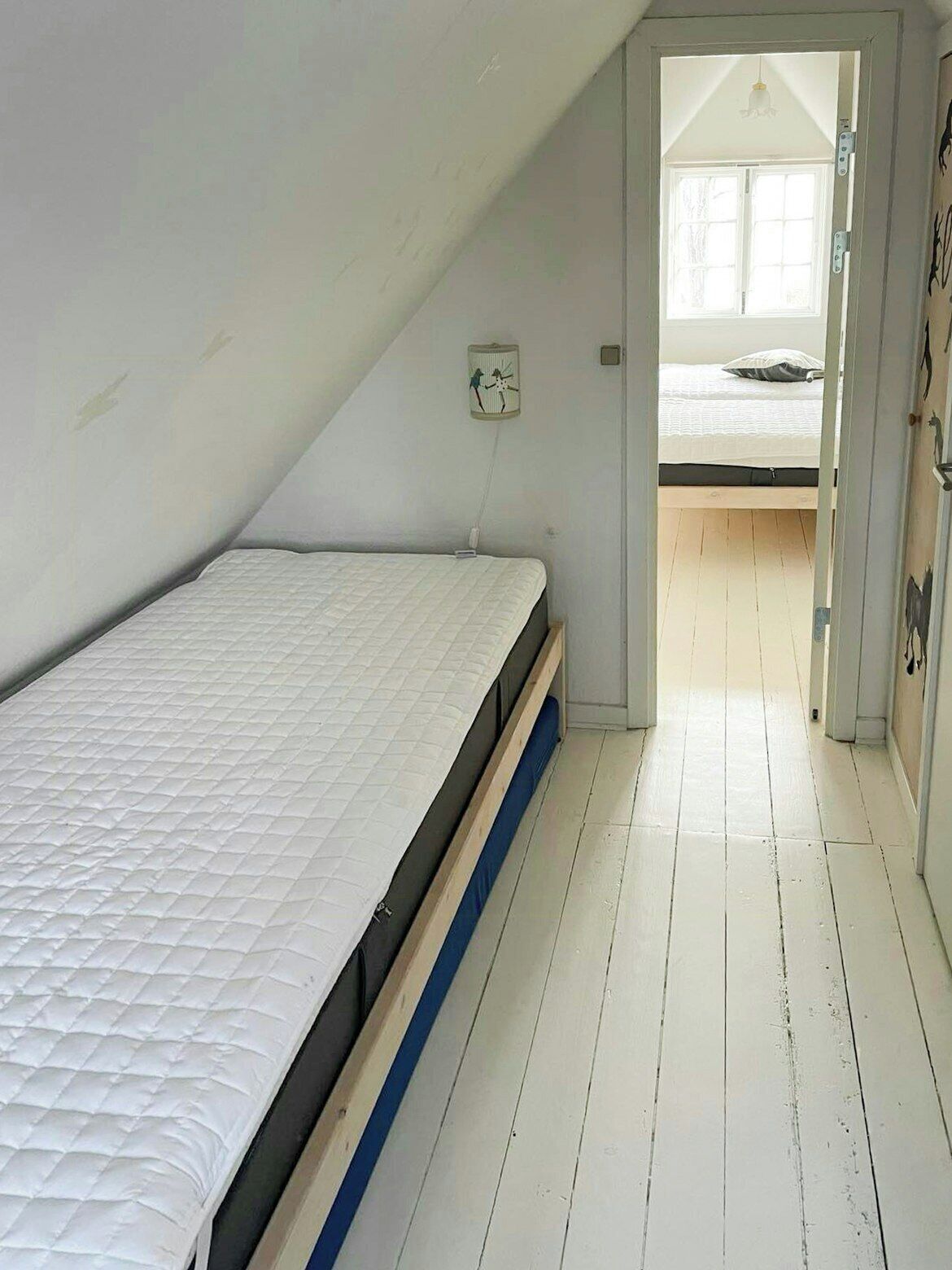A bedroom with a single bed, a small window, and a door leading to another room.