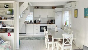 Eine moderne Küche mit weißen Schränken, einem Esstisch mit Stühlen und einer Treppe, die in einen oberen Bereich führt.