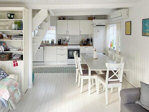 A modern kitchen with white cabinetry, a dining table with chairs, and a staircase leading to an upper level. - Thatched wooden house with sea view (Haderslev)
