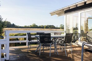 Una terraza de madera con mobiliario exterior, una cerca blanca y vistas a un campo.