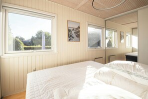 Un dormitorio con un ventanal grande, una cama, una mesita de noche y un espejo.