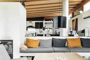 Ein modernes Wohnzimmer mit grauem Sofa, Holzboden und einer Küche im Hintergrund.
