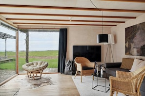 Ein modernes Wohnzimmer mit großem Fernseher, Korbmöbeln und Blick ins Freie.