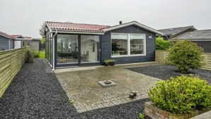Ein modernes, eingeschossiges Haus mit einem Ziegeldach, großen Glasfenstern und einer Schotterauffahrt.