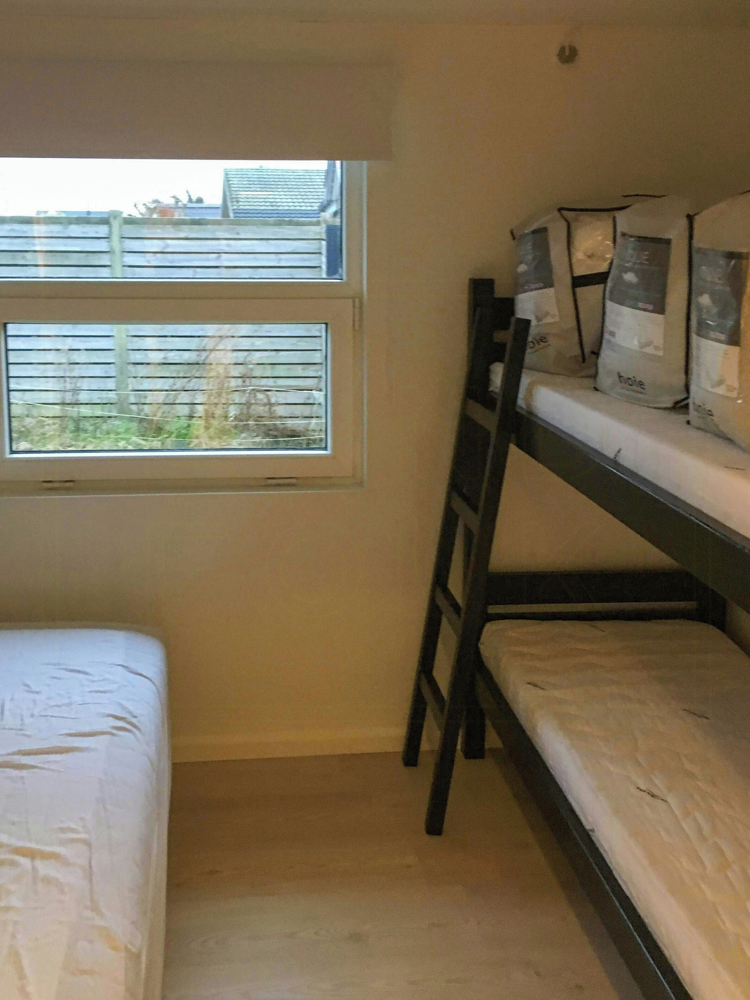 A bunk bed room with a window, a ladder, and bags on the bed.