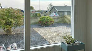 Ein Zimmer mit großem Fenster, einem Blumentopf und Blick auf einen Hinterhof mit Auto und Häusern.