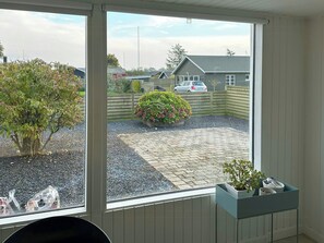 Ein Zimmer mit großem Fenster, einem Blumentopf und Blick auf einen Hinterhof mit Auto und Häusern.