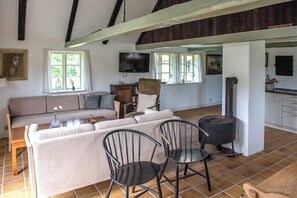 A living room with a sofa, chairs, a fireplace, a television, and a kitchen area. - ‘Knøv’ country retreat with seaweed roof on Læsø (Læsø)