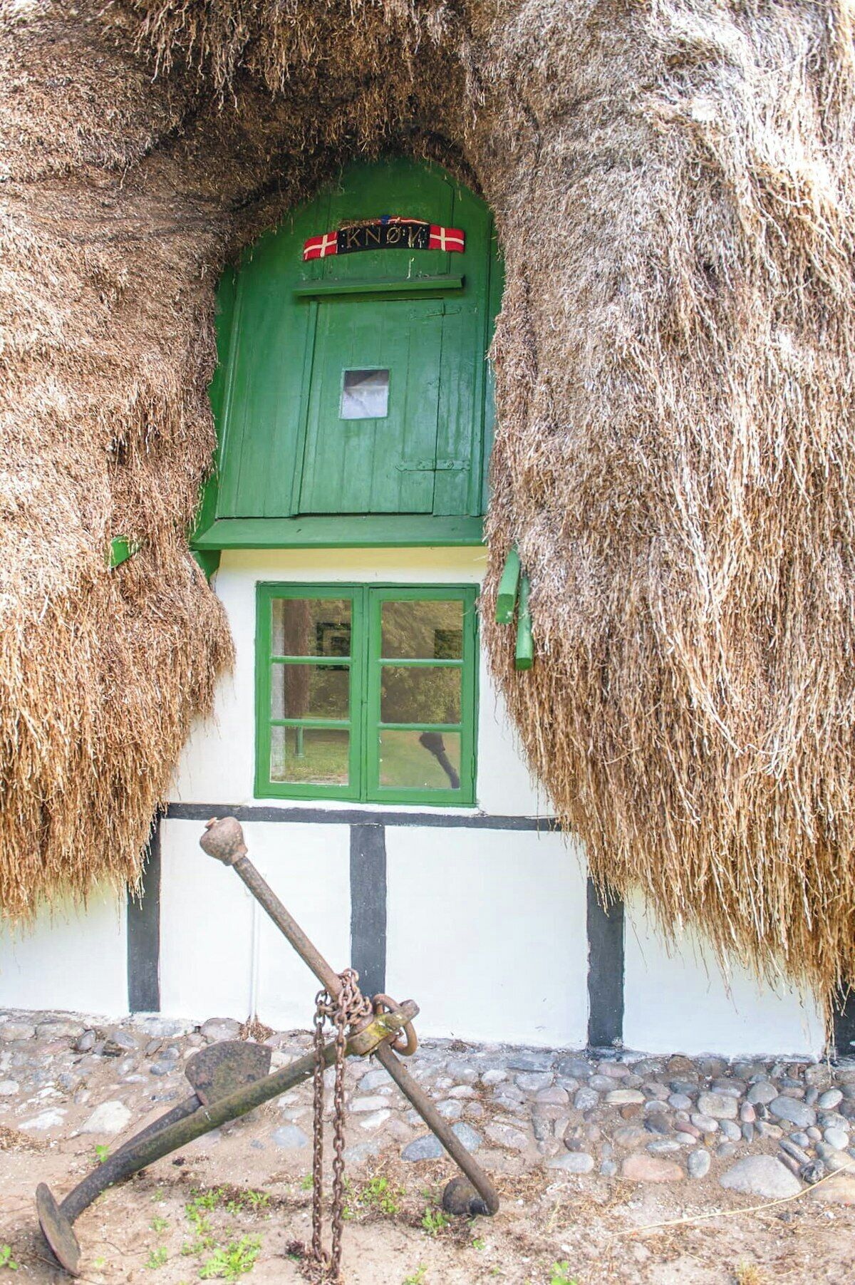 Ein traditionelles Haus mit einem Reetdach, einer grünen Tür und Fenstern, einem Steinfundament und einer rustikalen Atmosphäre.