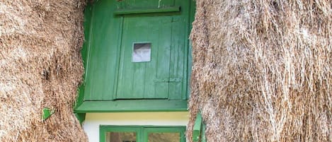 Ett traditionellt hus med halmtak, en grön dörr och fönster, en grund av sten och en rustik atmosfär.