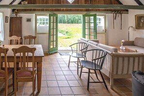 A rustic interior with a dining table, chairs, a sofa, and a view through open doors. - ‘Knøv’ country retreat with seaweed roof on Læsø (Læsø)