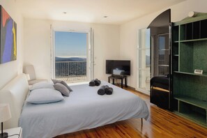 A bedroom with a bed, a TV, a balcony with a view, and a green shelving unit. - Villa with panoramic view over Cannes (Spéracèdes)
