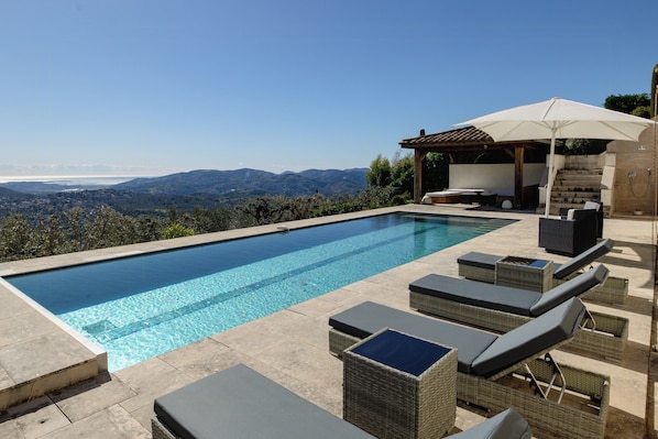 A swimming pool with lounge chairs and an umbrella, surrounded by a view of mountains. - Villa with panoramic view over Cannes (Spéracèdes)