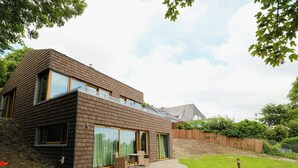 Een modern huis met twee verdiepingen, grote ramen, een terras en een keurig onderhouden tuin.