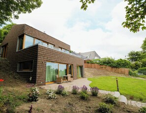 Ein modernes, zweistöckiges Haus mit großen Fenstern, einer Terrasse und einem gepflegten Garten.