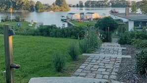 Een pad van stenen dat naar een gebied aan het meer leidt, met gebouwen en begroeiing.