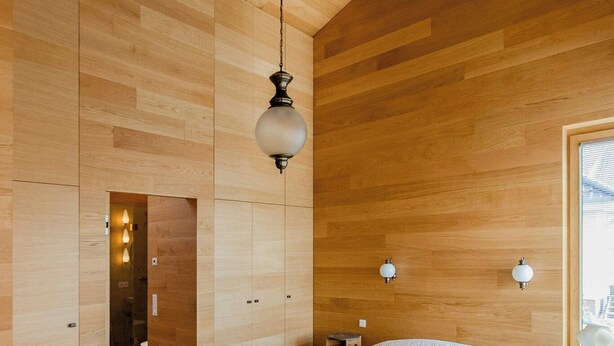 Een moderne slaapkamer met een groot bed, houten wanden, een hanglamp en uitzicht door een raam.