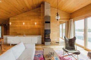 Ein modernes Wohnzimmer mit Holzboden, Kamin, einer Couch, einem Sessel und einem großen Fenster.