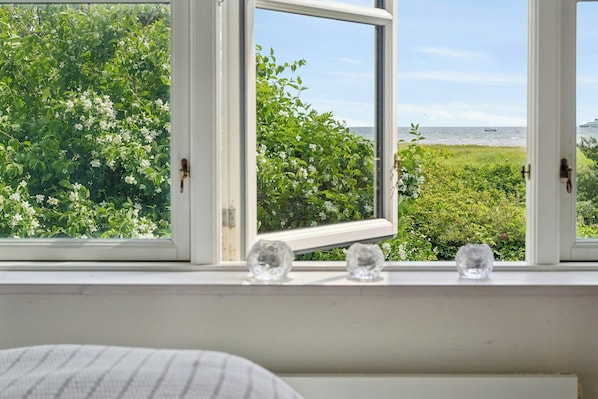 Ein Fenster mit Blick auf einen Garten und das Meer.
