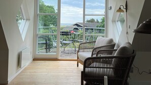 Une pièce avec un plafond en pente, de grandes fenêtres, des meubles en osier et une vue sur la verdure environnante.
