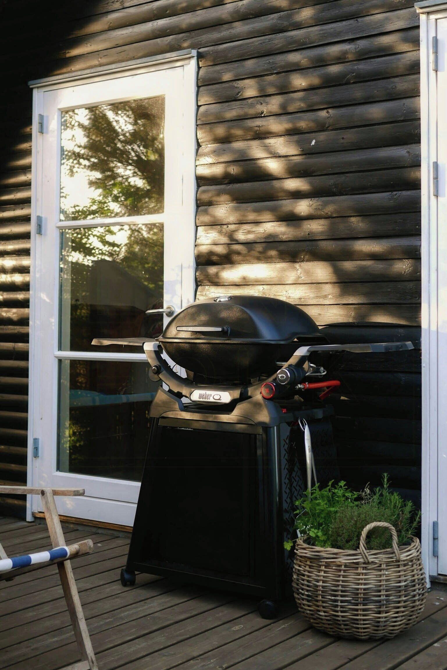 A portable grill on a wooden deck, a wicker basket with greenery, and a sliding glass door.