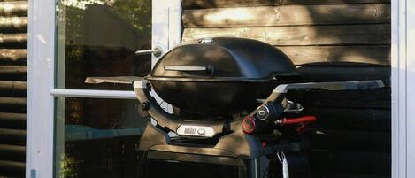 A portable grill on a wooden deck, a wicker basket with greenery, and a sliding glass door.