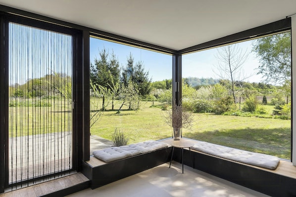 A modern room with large windows, a cushioned bench, and a small table. - Architectural house with views of Bornholm nature (Åkirkeby)