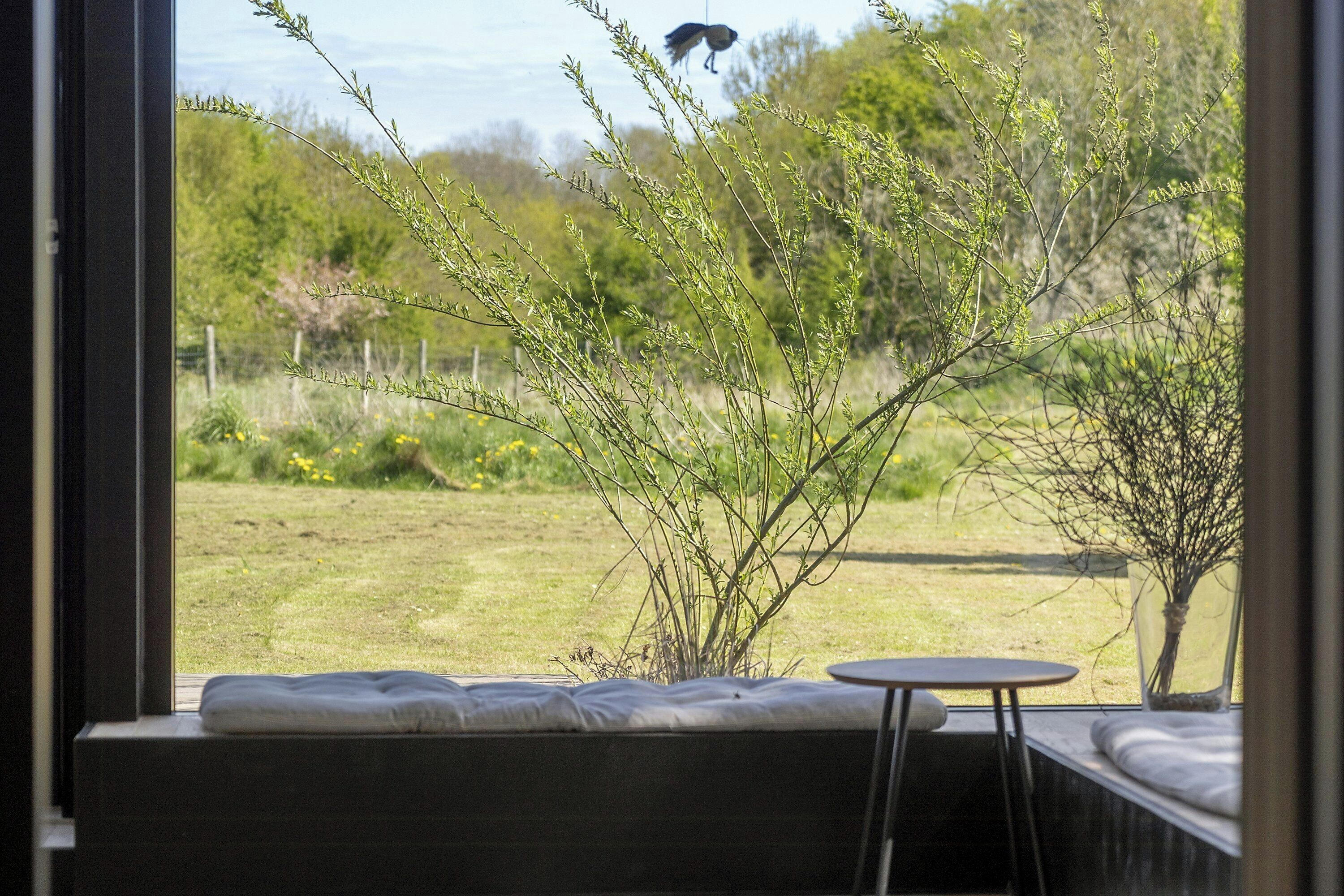 A room with a window overlooking a garden, a sofa, and a small round table.