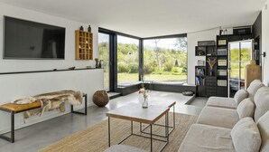 Ein modernes Wohnzimmer mit einem großen Flachbildfernseher, einer Holzbänkl mit Fell, einem Couchtisch und einer Couch.