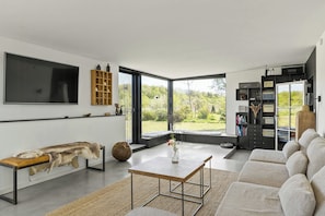 A modern living room with a large flat-screen TV, a wooden bench with fur, a coffee table, and a sofa. - Architectural house with views of Bornholm nature (Åkirkeby)