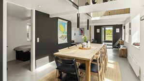 Ein modernes Interieur mit einem Holzesstisch, schwarzen Stühlen, einer schwarzen Couch und einer Treppe, die zu einem Schlafbereich führt.