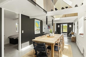 A modern interior with a wooden dining table, black chairs, a black sofa, and a staircase leading to a loft area. - Architectural house with views of Bornholm nature (Åkirkeby)