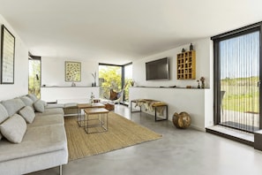A modern living room with a sectional sofa, a coffee table, a TV, and a large window. - Architectural house with views of Bornholm nature (Åkirkeby)