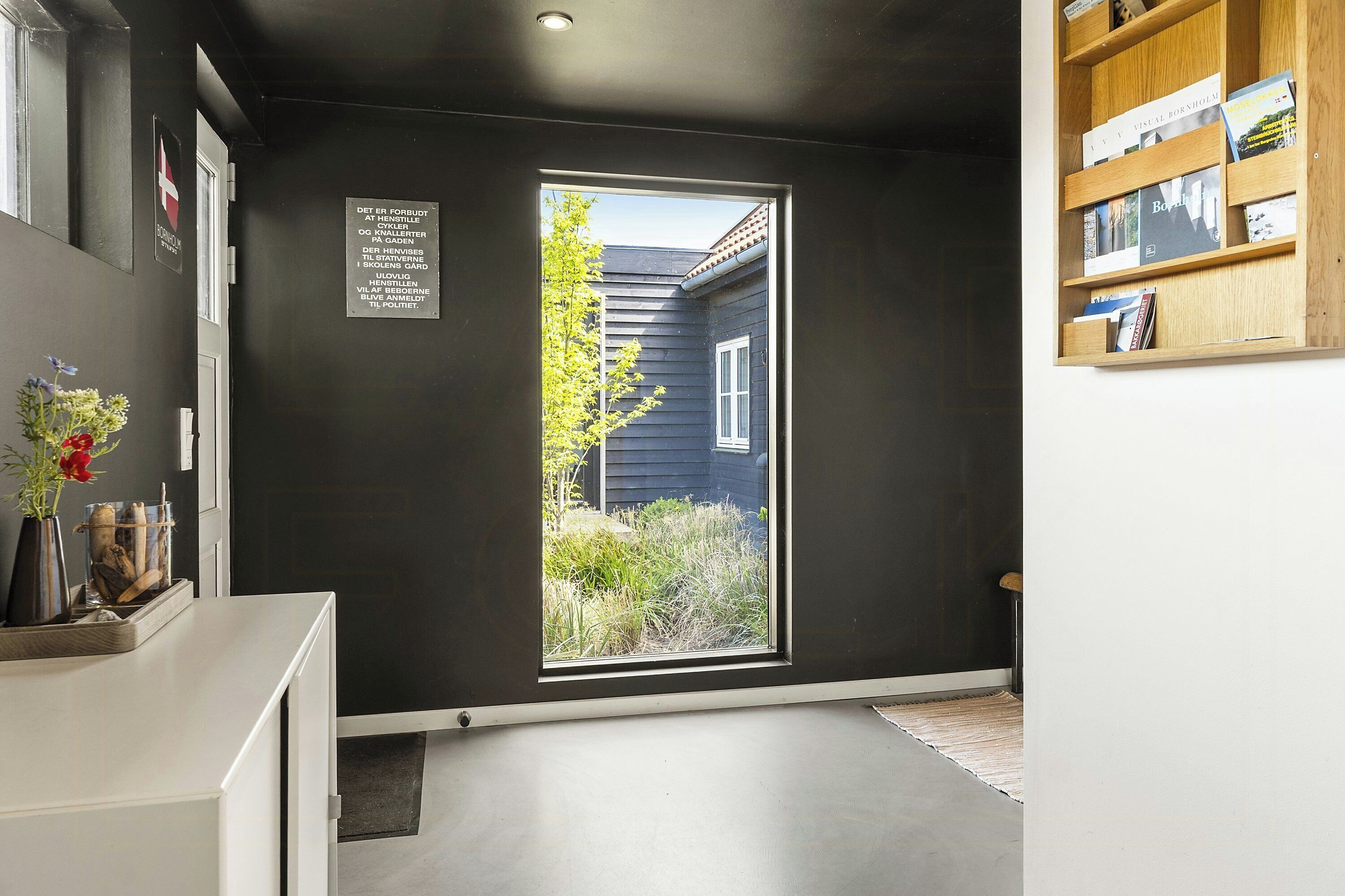 A room with a dark wall, a window with a view of a house, and a wooden bookshelf.