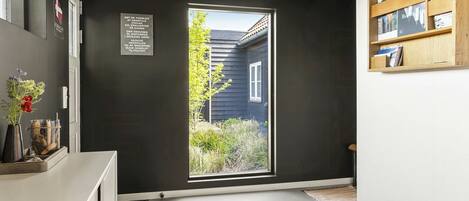 A room with a dark wall, a window with a view of a house, and a wooden bookshelf.