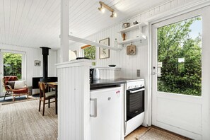 Una cocina compacta con horno empotrado, un refrigerador pequeño y una zona de comedor con una silla y una mesa.