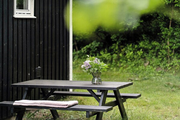 A picnic table with a vase of flowers, a bench, and a small building in the background. - Holiday home with view over Mols hills (Knebel)