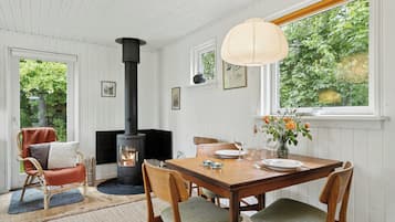 A cozy room with a fireplace, dining table, chairs, and a window with a view of greenery.