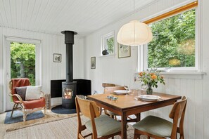 A cozy room with a fireplace, dining table, chairs, and a window with a view of greenery. - Holiday home with view over Mols hills (Knebel)