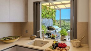 Cozinha com vista para uma varanda, churrasqueira e tábua de corte de madeira com legumes.
