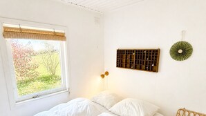 Makuuhuone, jossa on sänky, ikkuna, josta avautuu näkymä vehreään maisemaan, seinälle kiinnitetty hylly ja seinään asennettu valaisin.