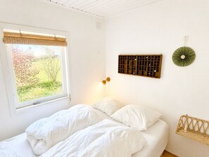 Et soveværelse med en seng, et vindue med udsigt til grønne områder, en vægmonteret hylde og en lampe.