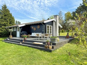 Et hus med en terrasse, udendørs møbler og plantekasser.