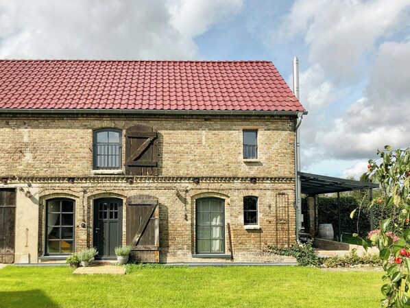 A two-story brick building with a red-tiled roof, multiple windows, and a small garden area.