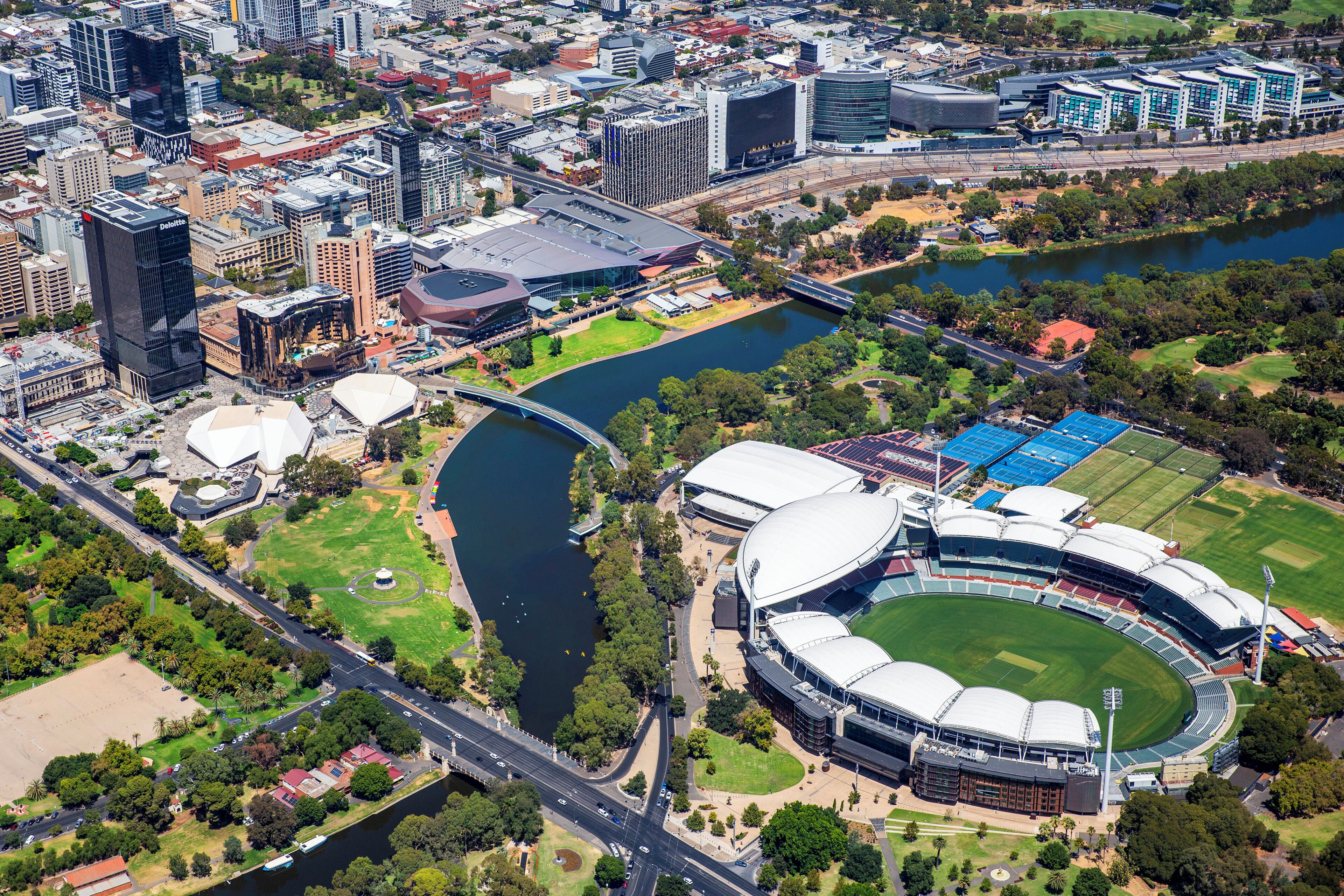 An aerial view of a stadium with a river, surrounding buildings, and a bridge.