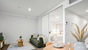 Ein modernes Wohnzimmer mit einer Couch, einem Esstisch mit Tellern und Besteck, einem kleinen runden Beistelltisch und einer großen Pflanze.