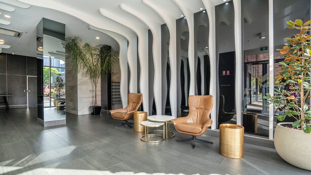 Eine moderne Lobby mit Ledersesseln, einem kleinen Tisch und einer großen Pflanze in einem Topf.